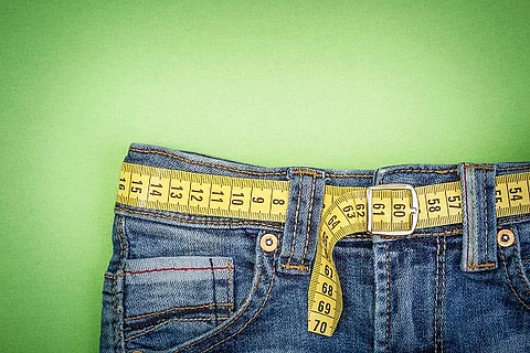 Ausschnitt einer Jeans mit Maßband als Gürtel auf grünem Hintergrund.