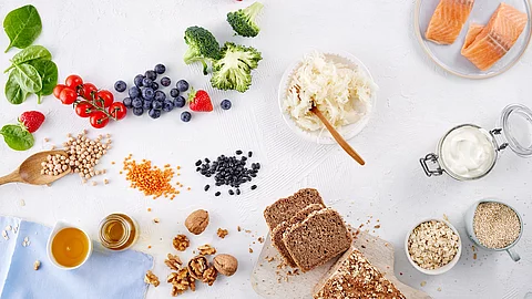 Tableau mit gesunden Lebensmitteln: Beeren, Broccoli, Haferflocken, Walnüsse, Lachs, Vollkornbrot, Linsen