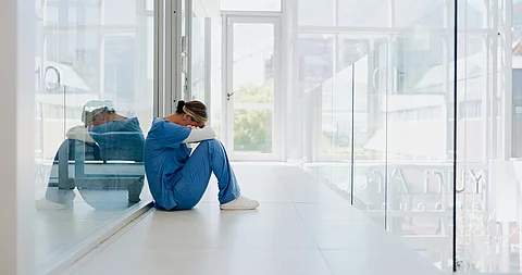 Ärztin sitzt auf dem Klinikboden und ist erschöpft nach ihrem Nachtdienst.