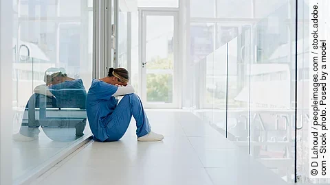 Ärztin sitzt auf dem Klinikboden und ist erschöpft nach ihrem Nachtdienst.