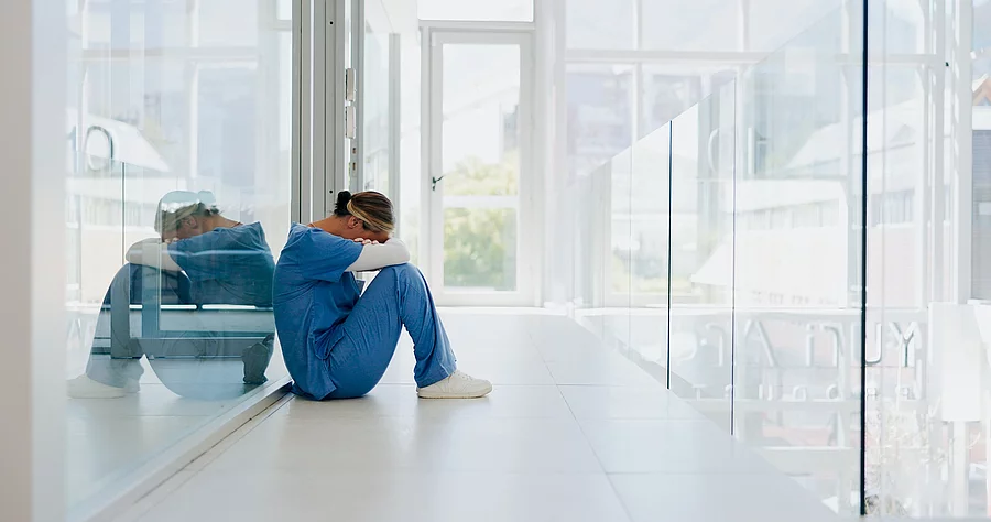Ärztin sitzt auf dem Klinikboden und ist erschöpft nach ihrem Nachtdienst.