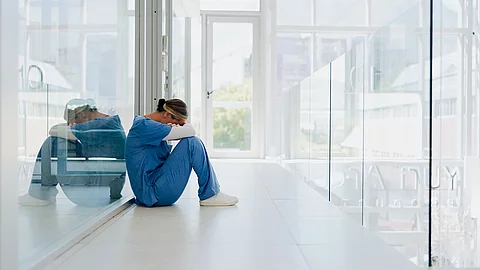 Ärztin sitzt auf dem Klinikboden und ist erschöpft nach ihrem Nachtdienst.