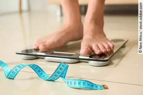 Person steht auf der Waage, daneben ein Maßband