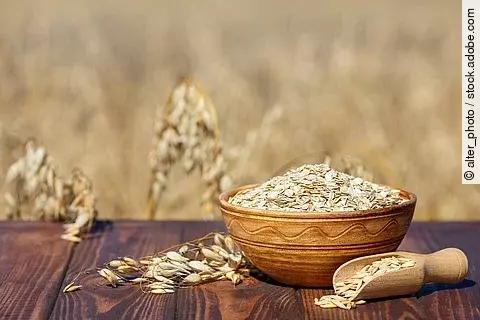 Haferflocken in Holzschale, daneben Haferrispe