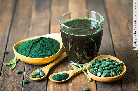 Grünes Algenpulver, Algenkapseln und aufgelöstes grünes Pulver in einem Glas, gruppiert auf Holzuntergrund