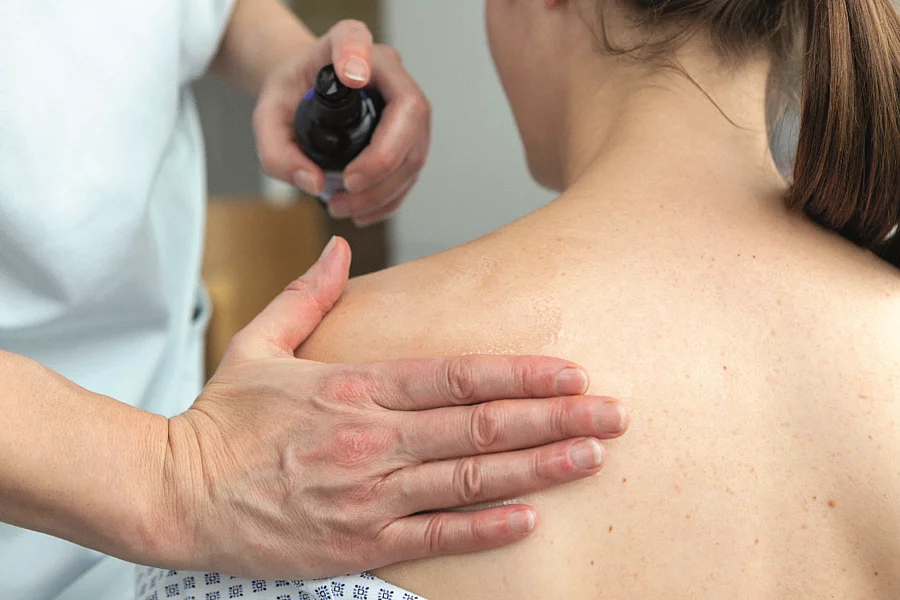 Pflegekraft reibt Patientin den Rücken mit einem Öl ein.