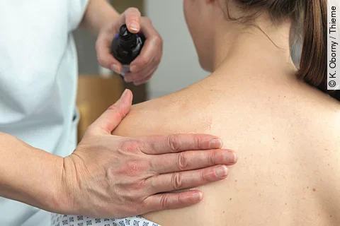 Pflegekraft reibt Patientin den Rücken mit einem Öl ein.