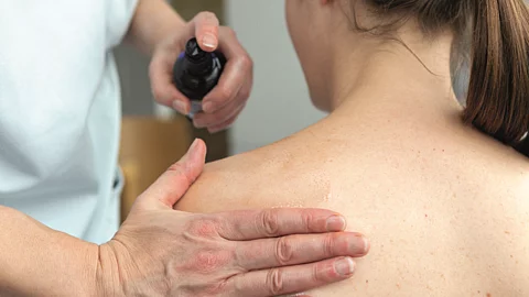 Pflegekraft reibt Patientin den Rücken mit einem Öl ein.