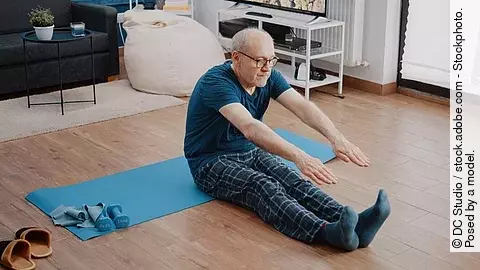 Senior macht Gymnastik im Schlafanzug auf Yogamatte im Wohnzimmer.