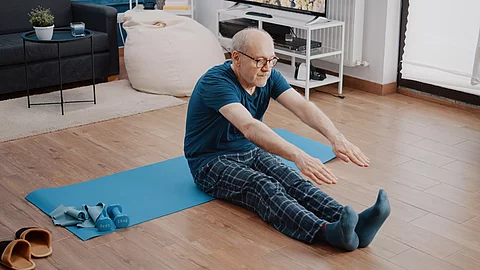 Senior macht Gymnastik im Schlafanzug auf Yogamatte im Wohnzimmer.