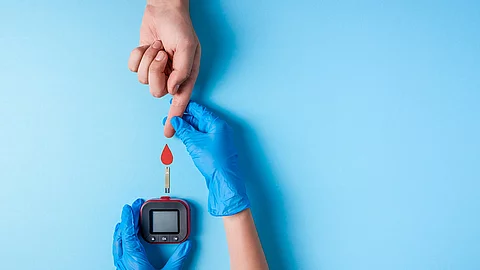Krankenschwester misst den Blutzucker, neben dem Messgerät ist ein Bluttropfen aus Papier.