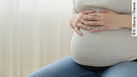 Sitzende Schwangere hat ihre Hände auf dem Bauch 