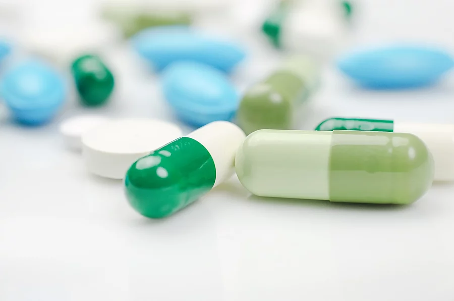 Blaue und grüne Tabletten und Kapseln auf weißem Hintergrund 