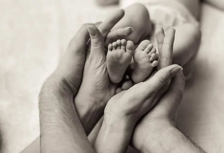 Mother holding tiny foot of newborn baby Eltern halten Babyfüße