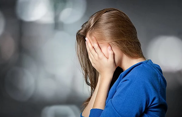 Frau mit braunen Haaren hält sich die Hände vor ihr Gesicht.