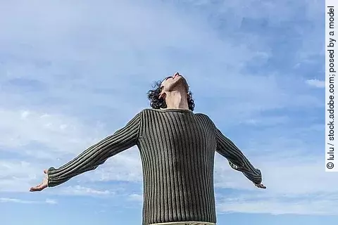 Mann streckt die Arme nach hinten, im Hintergrund ist der blaue Himmel zu sehen.