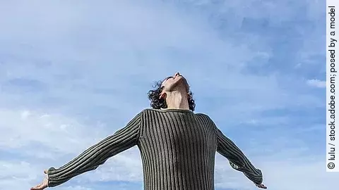 Mann streckt die Arme nach hinten, im Hintergrund ist der blaue Himmel zu sehen.