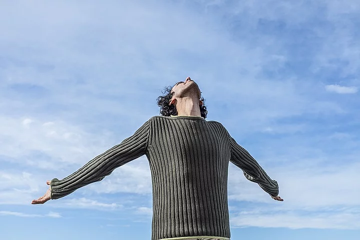 Mann streckt die Arme nach hinten, im Hintergrund ist der blaue Himmel zu sehen.