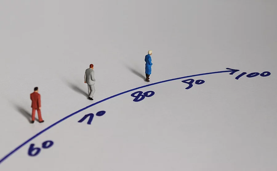 Illustration: 3 Menschen laufen auf einer Linie mit Zahlen zwischen 60 und dem Ziel 100 Jahre