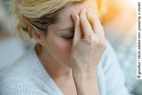 Blonde Frau fasst sich an die Stirn, da sie vermutlich Kopfschmerzen hat.