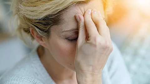Blonde Frau fasst sich an die Stirn, da sie vermutlich Kopfschmerzen hat.