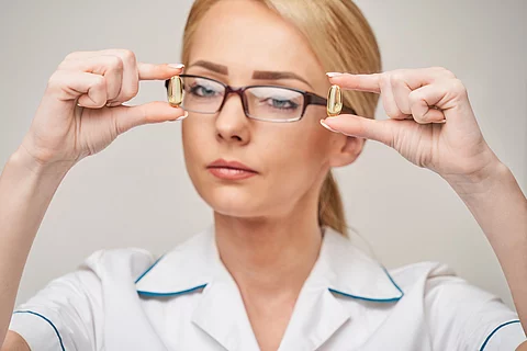 Blonde Frau mit Brille hält zwei Omega-3 Kapseln in den Händen.
