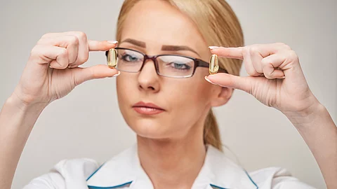 Blonde Frau mit Brille hält zwei Omega-3 Kapseln in den Händen.