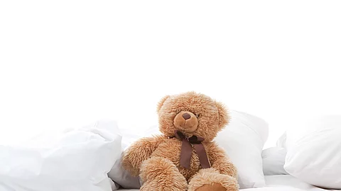 Teddybär sitzt auf einem Bett mit weißen Laken.