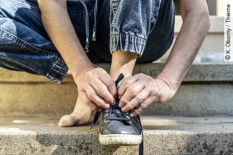 Frau mit geschwollenen Fingergelenken beim Schuhe zubinden