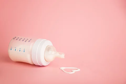 Flasche mit Muttermilch und Herz aus Muttermilch auf rosa Hintergrund.