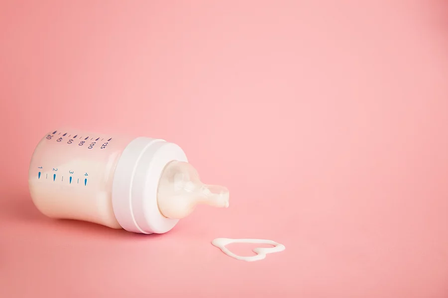 Flasche mit Muttermilch und Herz aus Muttermilch auf rosa Hintergrund.