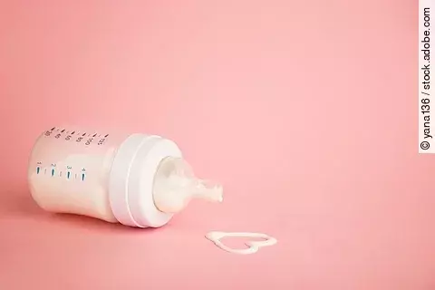 Flasche mit Muttermilch und Herz aus Muttermilch auf rosa Hintergrund.