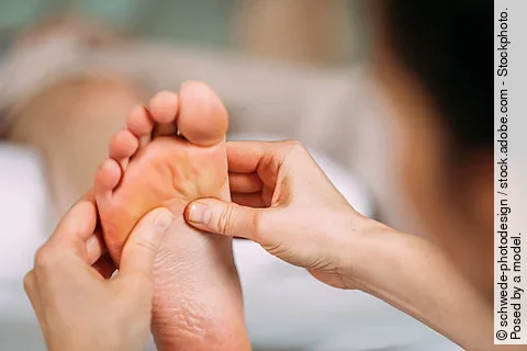 Eine Therapeutin massiert einen Fuß.