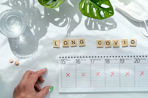 Ausdruck Long COVID aus Holzbuchstaben gelegt. Darunter liegt ein Wochenplaner.