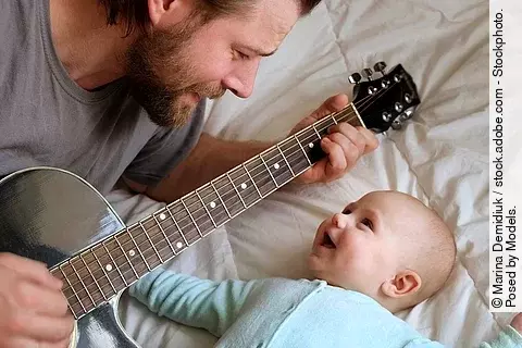 Vater spielt seinem lachenden Baby auf der Gitarre vor 