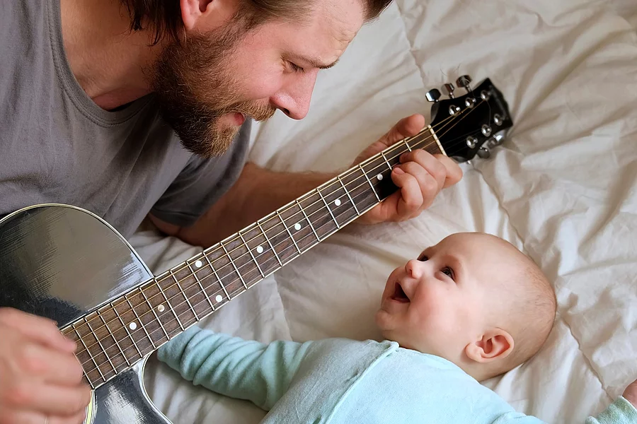 Vater spielt seinem lachenden Baby auf der Gitarre vor Vater spielt seinem lachenden Baby auf der Gitarre vor
