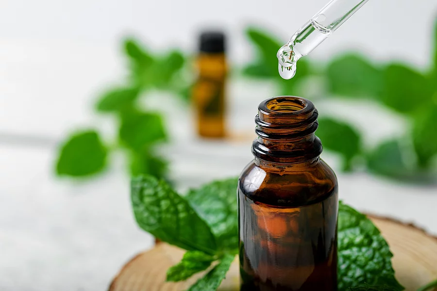 mint essential oil drop falling from dropper into the bottle Braunfläschchen mit Pfefferminzöl und frische Minze auf Holztisch