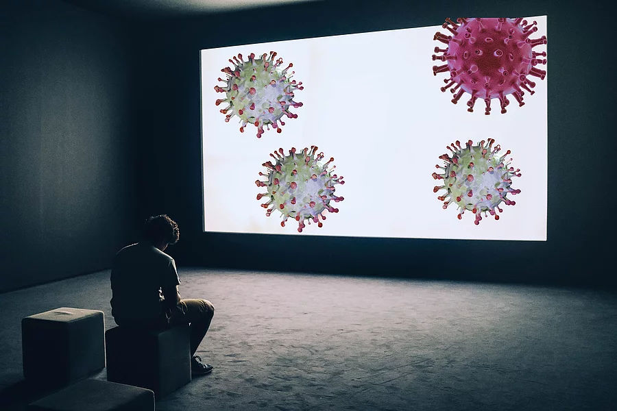 gebeugt sitzender Mann vor einer Leinwand mit Coronaviren
