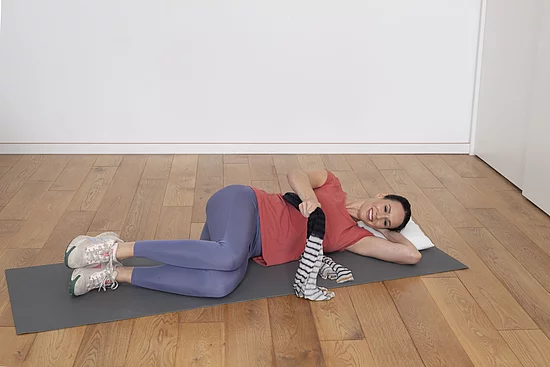 Junge Frau liegt seitlich auf Yogamatte und macht Atemübungen.