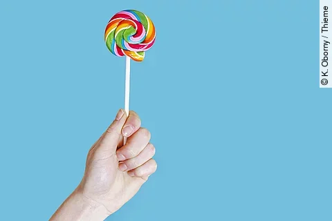 Hand hält bunten Lutscher in die Höhe