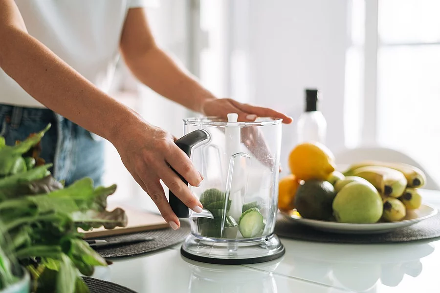Junge Frau steht in der Küche und bereitet einen Smoothie aus Gurken vor