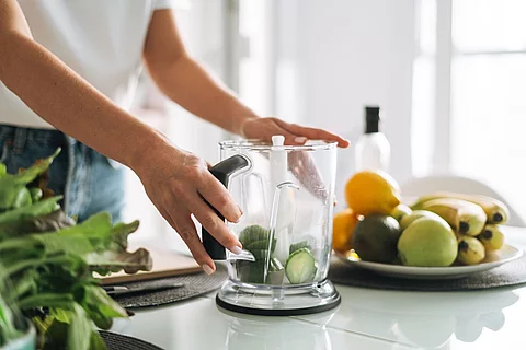 Junge Frau steht in der Küche und bereitet einen Smoothie aus Gurken vor