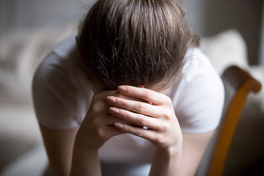 Close up desperate woman sitting on chair crying at home junge Frau mit den Händen vor dem Gesicht, traurig