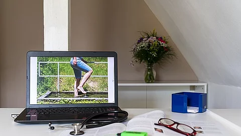 Symbolbild Integrative Medizin, Arztschreibtisch mit Stethoskop und Laptop mit Bild zu Kneipp-Wassertreten