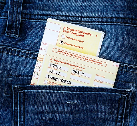 Formular mit Long Covid Krankmeldung steckt in der Hosentasche einer Jeans