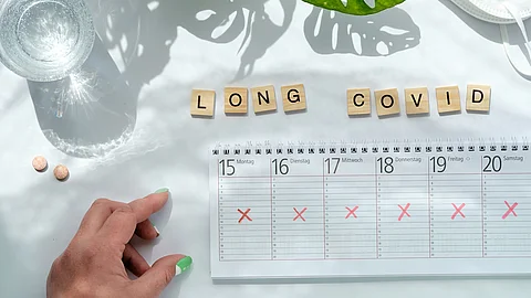Holzklötzchen mit der Aufschrift Long Covid, daneben ein ausgekreuzter Kalender 