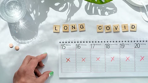 Holzklötzchen mit der Aufschrift Long Covid, daneben ein ausgekreuzter Kalender 