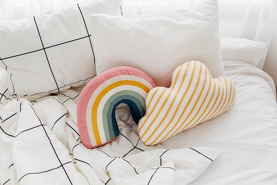 Bett mit weißer Bettwäsche und bunten kleinen Kissen