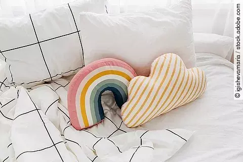 Bett mit weißer Bettwäsche und bunten kleinen Kissen