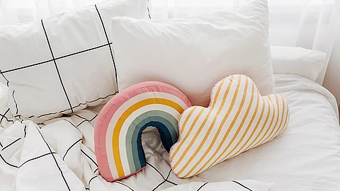 Bett mit weißer Bettwäsche und bunten kleinen Kissen